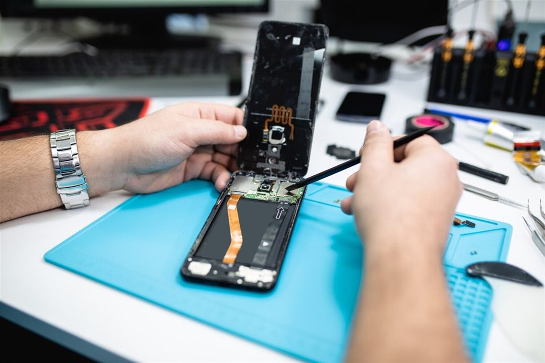 Técnico abrindo um celular sobre o tapete de reparo na bancada